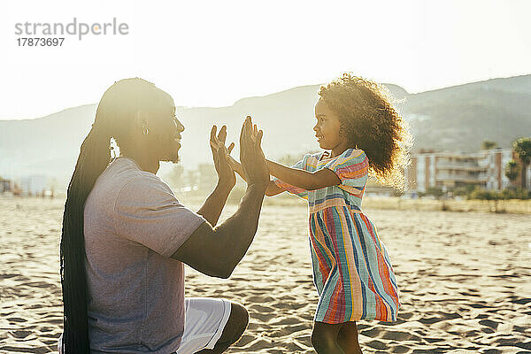 Lächelnder Mann spielt mit seiner Tochter am Strand ein Klatschspiel