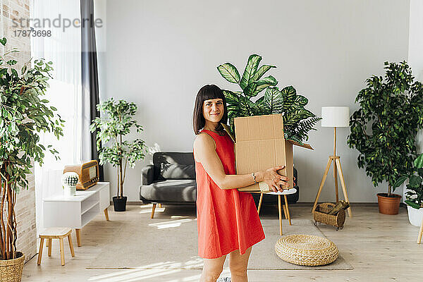 Lächelnde Frau trägt eine Kiste im Wohnzimmer