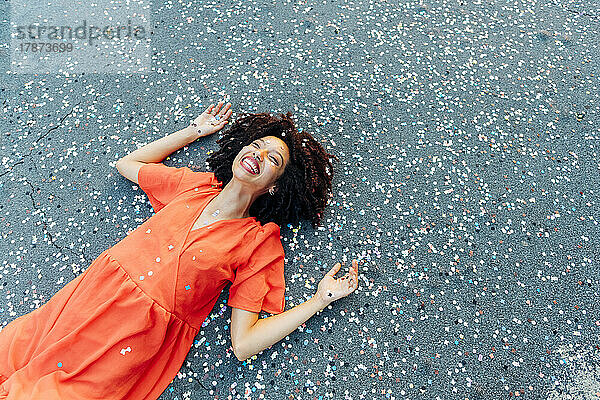 Glückliche junge Frau mit Konfetti auf der Straße liegend