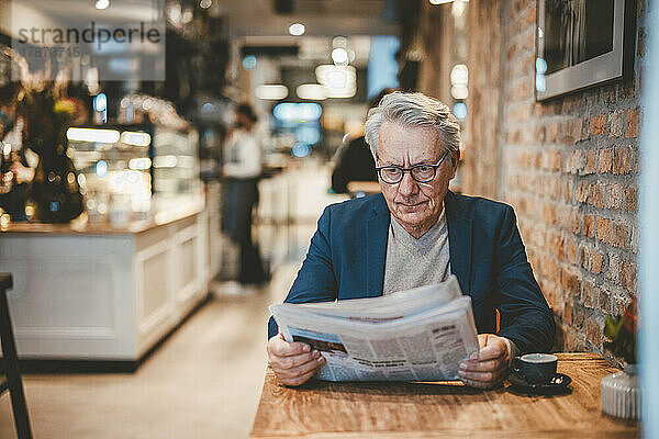 Leitender Geschäftsmann liest Zeitung im Café