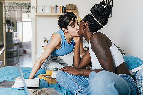 Lesbian couple kissing each other on bed at home