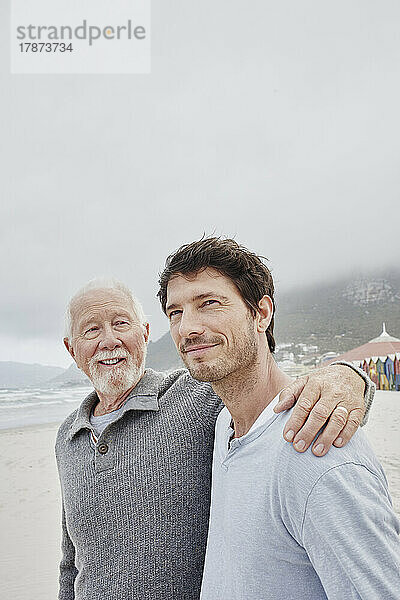 Stolzer Vater steht mit seinem erwachsenen Sohn am Strand