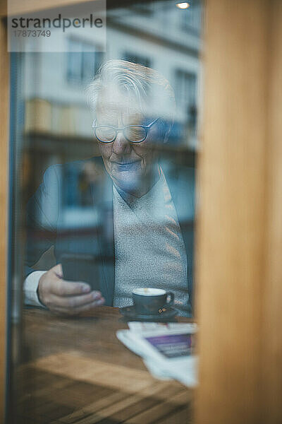 Geschäftsmann benutzt Mobiltelefon  gesehen durch das Fenster eines Cafés