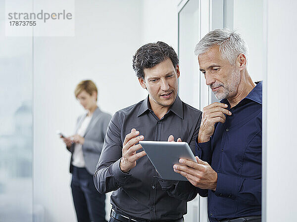 Geschäftsmann und Kollege diskutieren über Tablet-PC vor der Tür im Büro