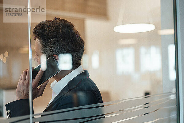 Businessman talking on smart phone seen through glass in office