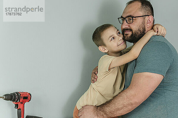 Happy father embracing son in front of wall