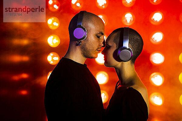 Affectionate couple with headphones by red illuminated lighting