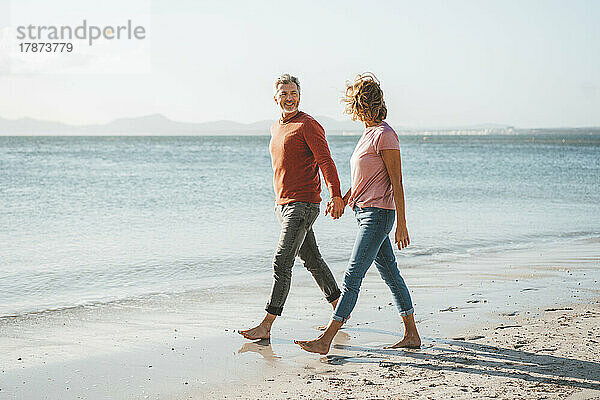 Glückliches älteres Paar  das Händchen haltend am Ufer des Strandes spaziert