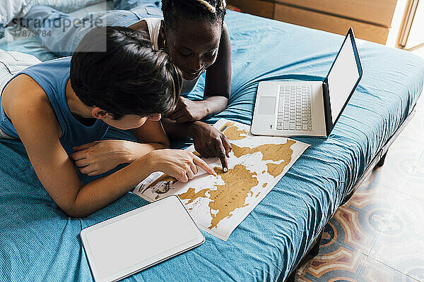 Young lesbian couple planning trip with map on bed at home