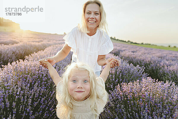 Glückliche Mutter spielt mit Tochter im Lavendelfeld bei Sonnenuntergang