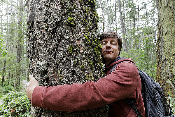 Mann mit geschlossenen Augen umarmt Baum im Wald