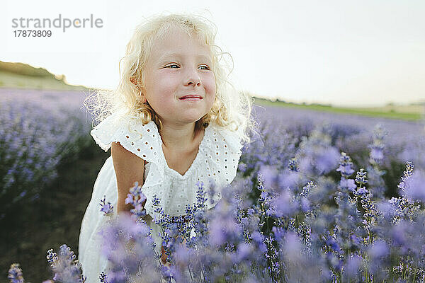 Lächelndes süßes Mädchen  das inmitten von Lavendelpflanzen steht