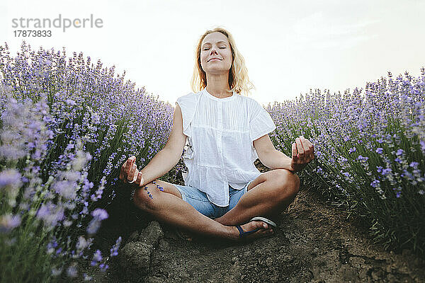 Lächelnde Frau meditiert inmitten von Lavendelpflanzen