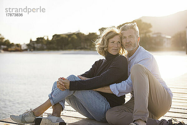 Glückliches älteres Paar  das an einem sonnigen Tag auf dem Steg sitzt