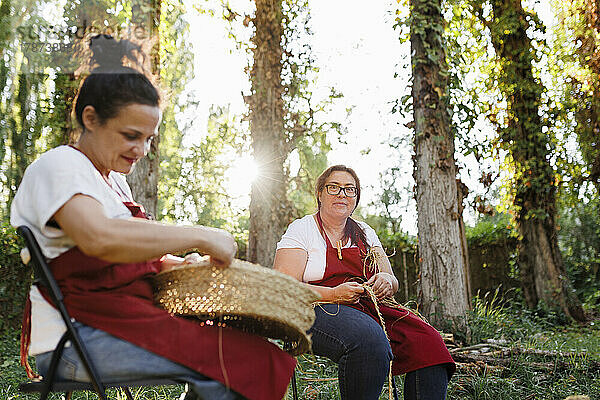 Lächelnder Kunsthandwerker mit Kollege beim Weben von Espartogras im Garten