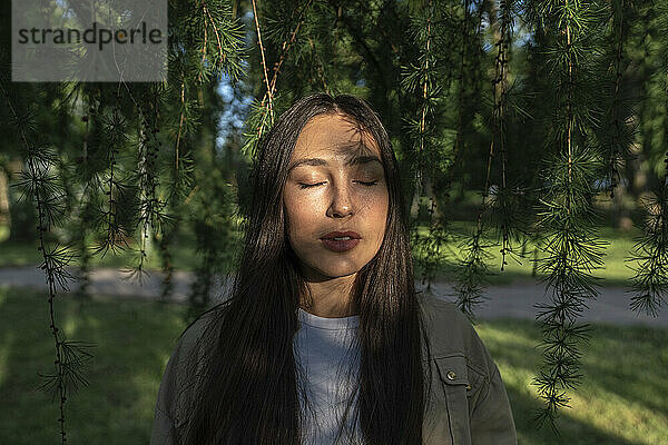 Frau mit geschlossenen Augen steht an einem sonnigen Tag im Park