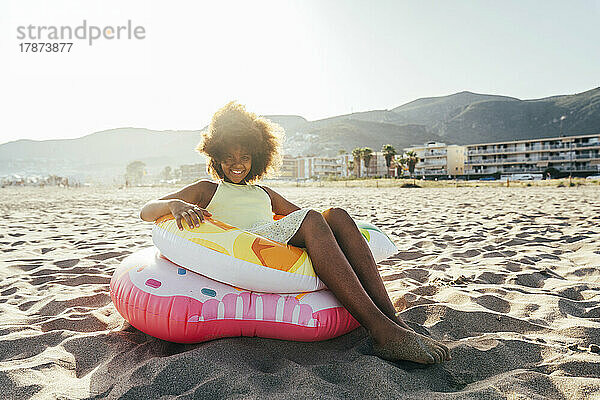Glückliches Mädchen  das auf einem aufblasbaren Ring am Strand sitzt
