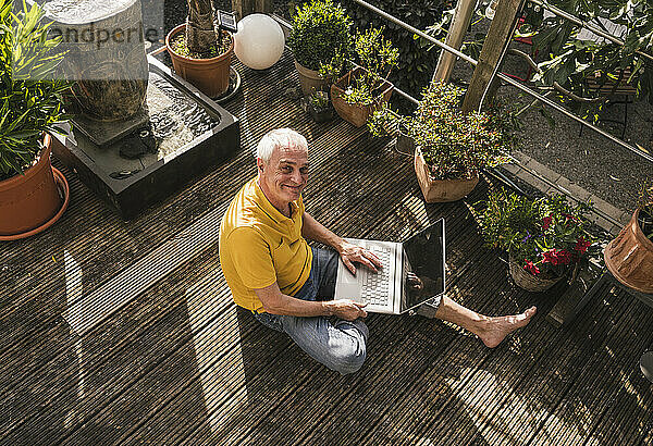 Lächelnder Mann mit Laptop sitzt auf der Terrasse