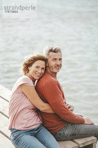 Glückliche Frau mit Mann sitzt auf dem Steg vor dem Meer