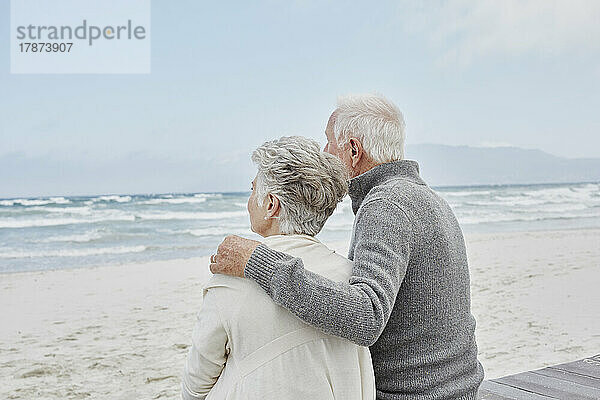 Älteres Paar steht mit Armen am Strand