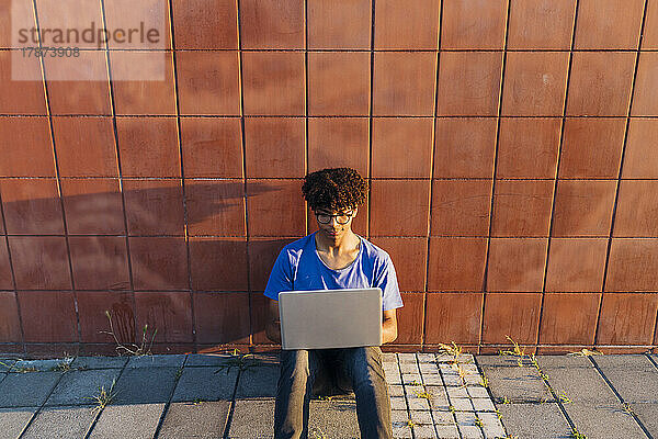 Young man using laptop for studying sitting leaning on wall