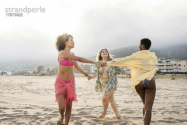 Gemischtrassige Frauen in Badebekleidung spielen am Strand um die Rose herum