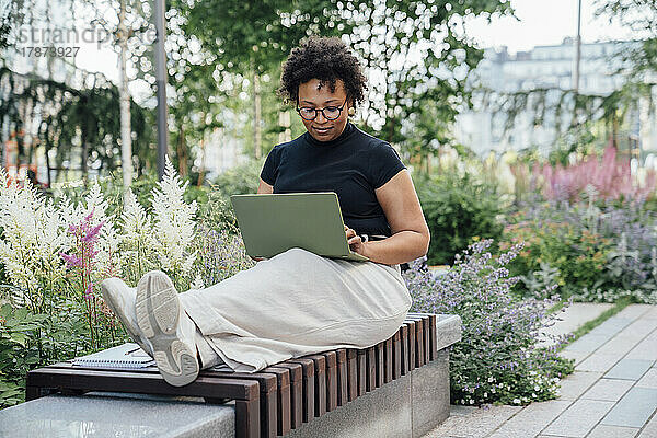 Smiling businesswoman using laptop sitting on bench