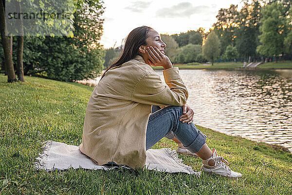 Frau sitzt mit der Hand am Kinn am See im Park