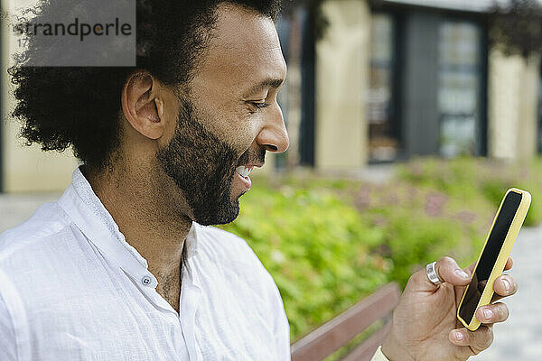 Glücklicher Mann mit Bart  der sein Mobiltelefon benutzt