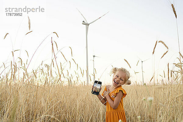 Fröhliches Mädchen mit Smartphone im Weizenfeld