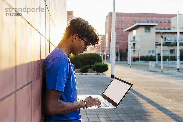 Junger Mann studiert mit Laptop  der an die Wand gelehnt ist