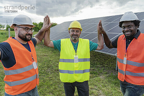 Lächelnde Ingenieure geben sich gegenseitig High Five im Solarkraftwerk