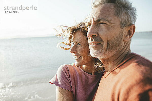 Lächelnder reifer Mann mit Frau am Strand an einem sonnigen Tag
