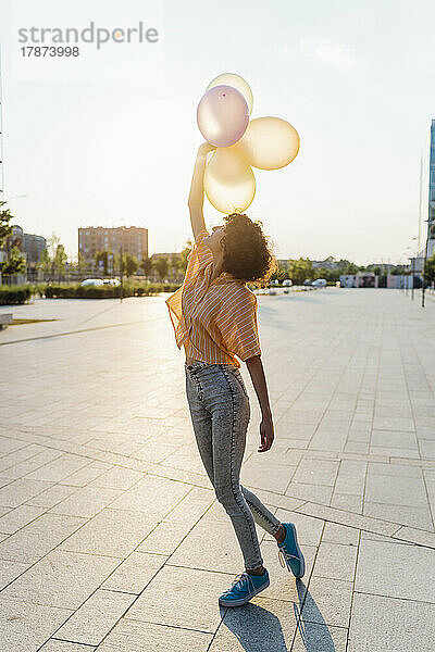 Young woman with hand raised holding balloons