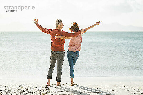 Älteres Paar mit ausgestreckten Armen steht am Ufer am Strand