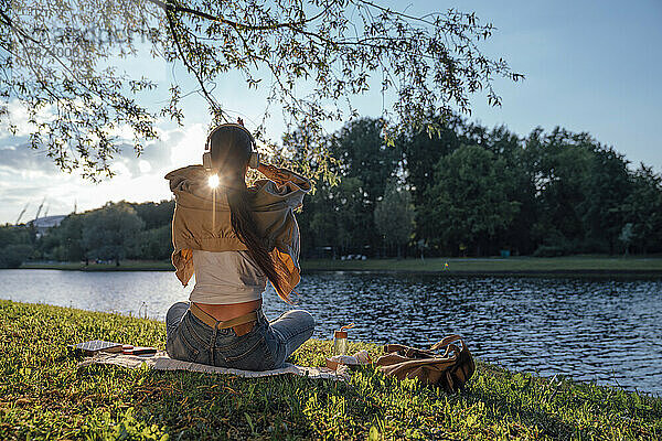 Frau sitzt mit Kopfhörern auf Gras am See im Park