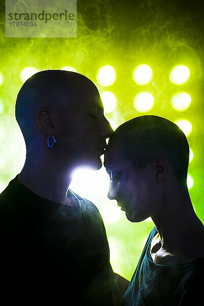 Man kissing on woman's forehead by neon lighting