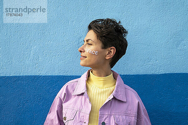 Frau mit Friedenstext auf der Wange vor blauer Wand