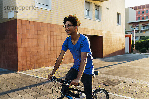 Lächelnder Mann  der bei Sonnenuntergang Fahrrad in der Stadt fährt