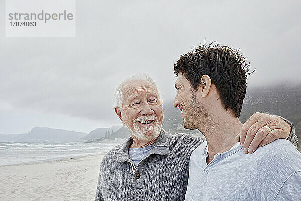 Stolzer Vater steht mit seinem erwachsenen Sohn am Strand