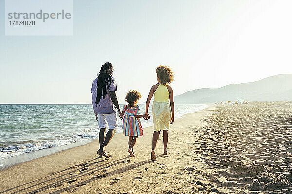 Mann mit Töchtern geht an sonnigem Tag am Strand spazieren