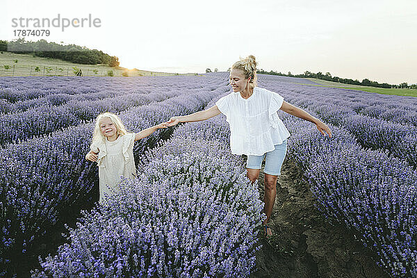 Happy mother with daughter holding hand walking in lavender field