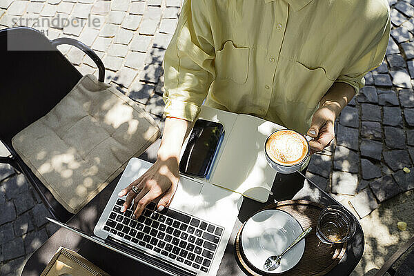 Freiberufler mit Kaffeetasse arbeitet am Laptop und sitzt im Straßencafé