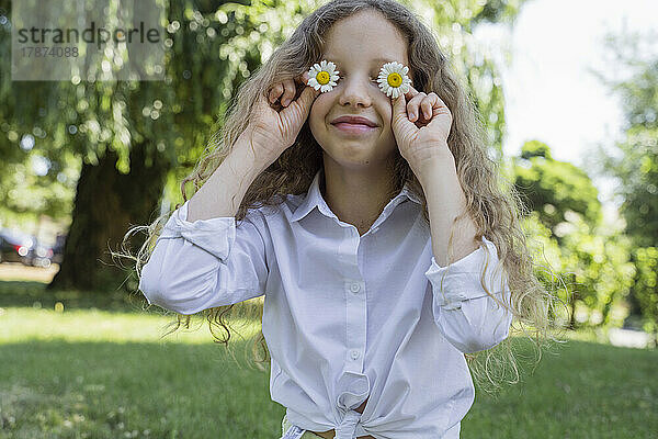 Lächelndes Mädchen  das die Augen mit Kamillenblüten bedeckt