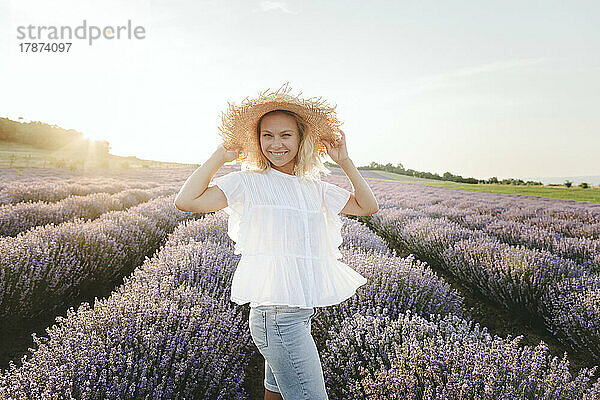 Glückliche Frau mit Hut steht im Lavendelfeld