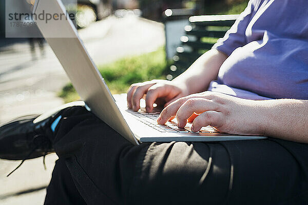 Hände eines Teenagers  der im Park einen Laptop benutzt