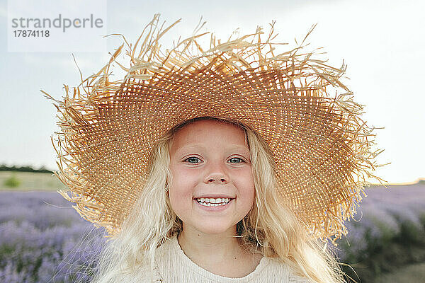 Happy girl wearing straw hat standing in lavender field