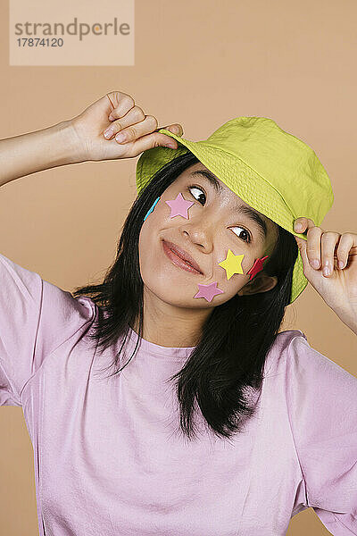 Lächelnde junge Frau mit Sternen im Gesicht und gelbem Fischerhut