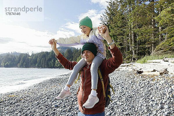 Vater trägt Tochter auf Schultern am Strand