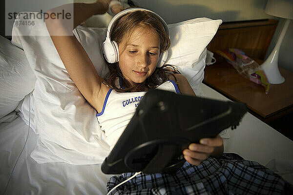 Girl with hand raised wearing headphones using tablet PC relaxing on bed in motorboat